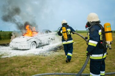 firemen spraying on flaming vehicle for training. Volunteer firefighters do not get paid in alberta canada.