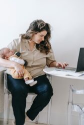 mother with baby using laptop for work from home. We answer “can you work while on maternity leave in alberta, canada?”