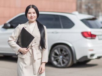 Woman insurance agent in front of car. Alberta has private auto insurance.