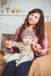 woman wearing red and white plaid shirt sitting on chair holding baby. We talk about how old you have to be to babysit in Alberta, Canada.