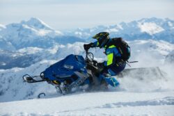 man in blue and green long sleeved suit riding on snowmobile in Alberta mountains. Where can you snowmobile in Alberta?