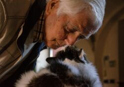 man in black and white jacket holding white and black cat. What is the Alberta Seniors benefit in Alberta canada?