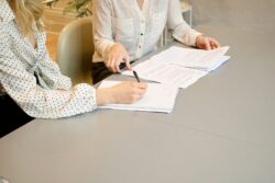 woman signing on white printer paper beside woman about to touch the documents. What is spousal support in alberta canada?